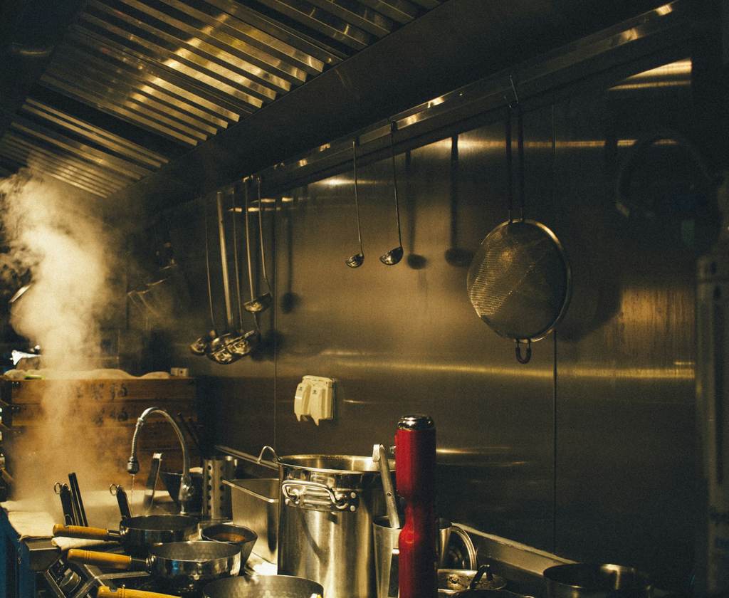 Steam rising under a stainless steel exhaust hood in a commercial kitchen