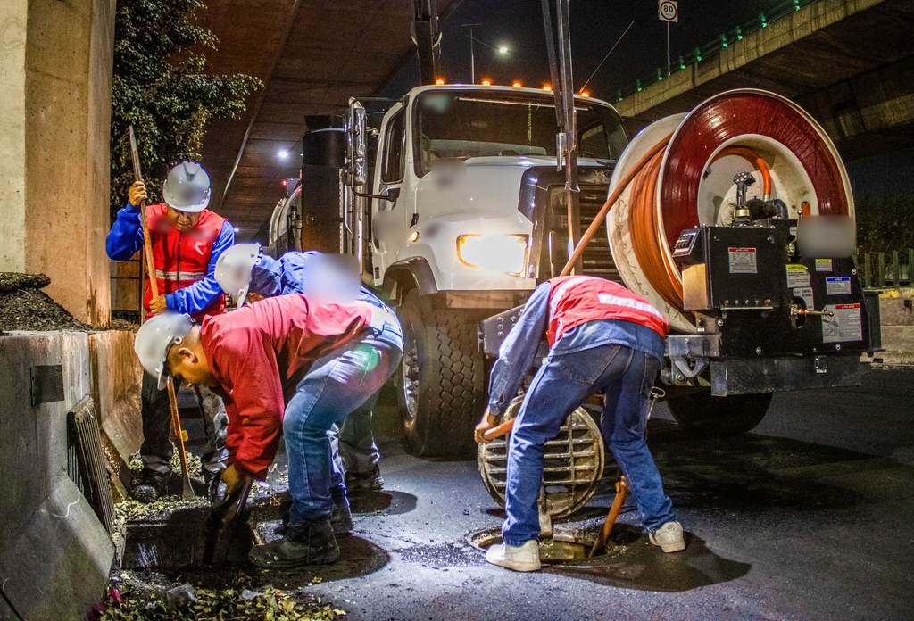 Crew cleaning a storm drain next to a vacuum truck at night